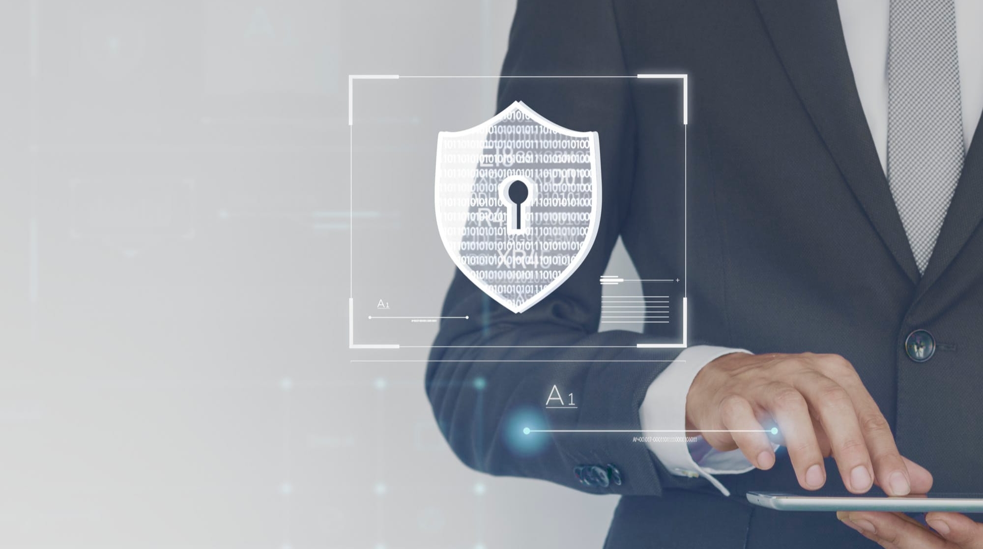 Mężczyzna w garniturze trzyma tablet, na ekranie widoczny symbol tarczy z kłódką